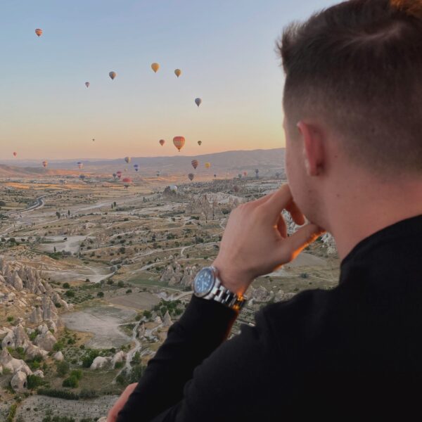 Globo aerostático elevándose sobre el paisaje de Capadocia durante el amanecer, con formaciones rocosas y chimeneas de hadas iluminadas por la luz dorada.