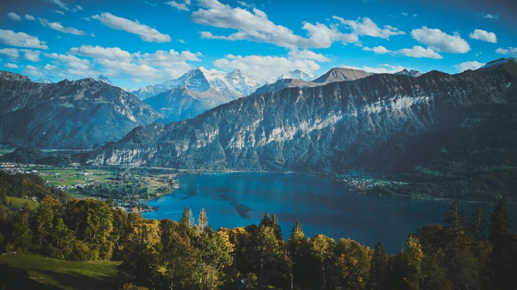 Panorámica de un lago en Interlaken, Suiza, rodeado de montañas con nieve en el pico y vegetación